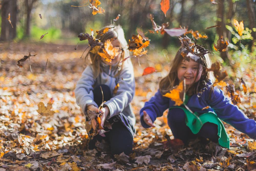 Kaksi pientä tyttöä leikki syksyn värikkäillä lehdillä.