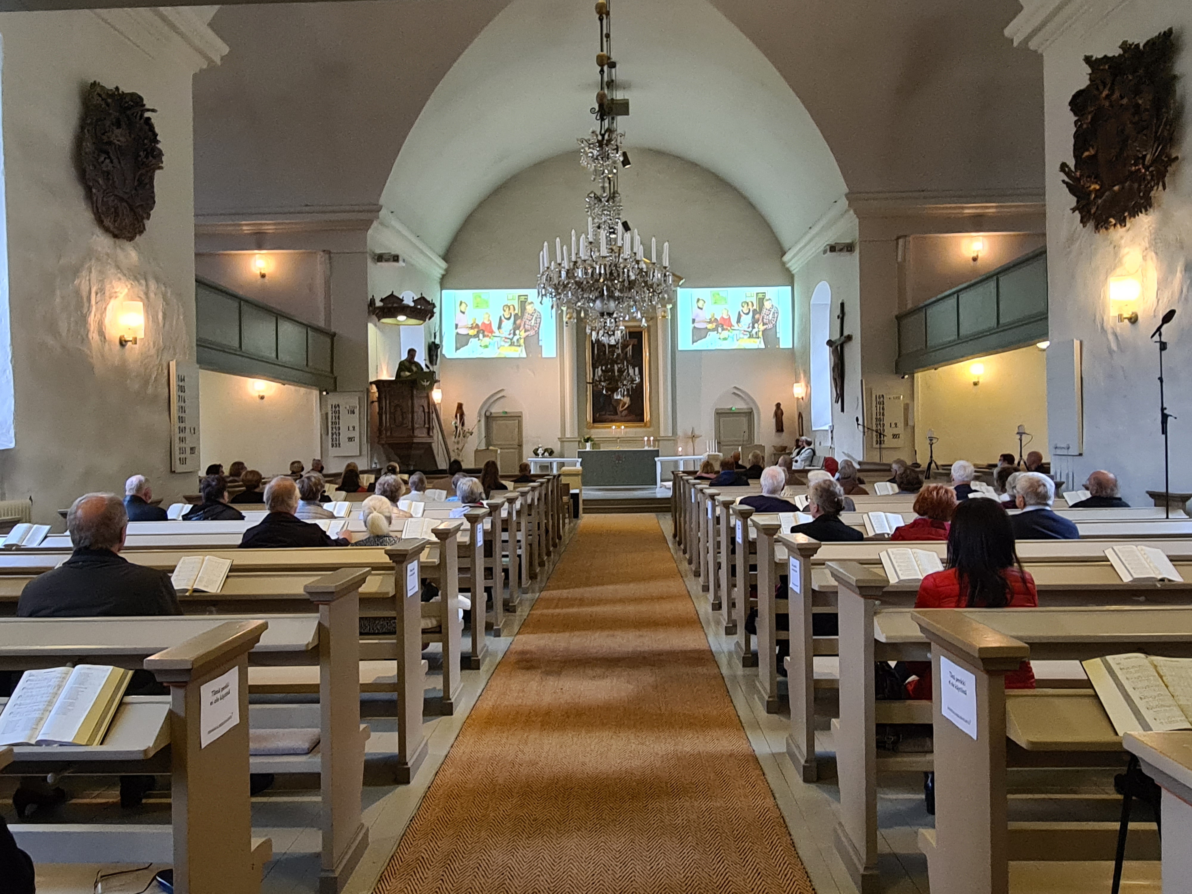 Messuväki kuuntelee saarnaa ja katselee valokuvia vuosien varrelta.